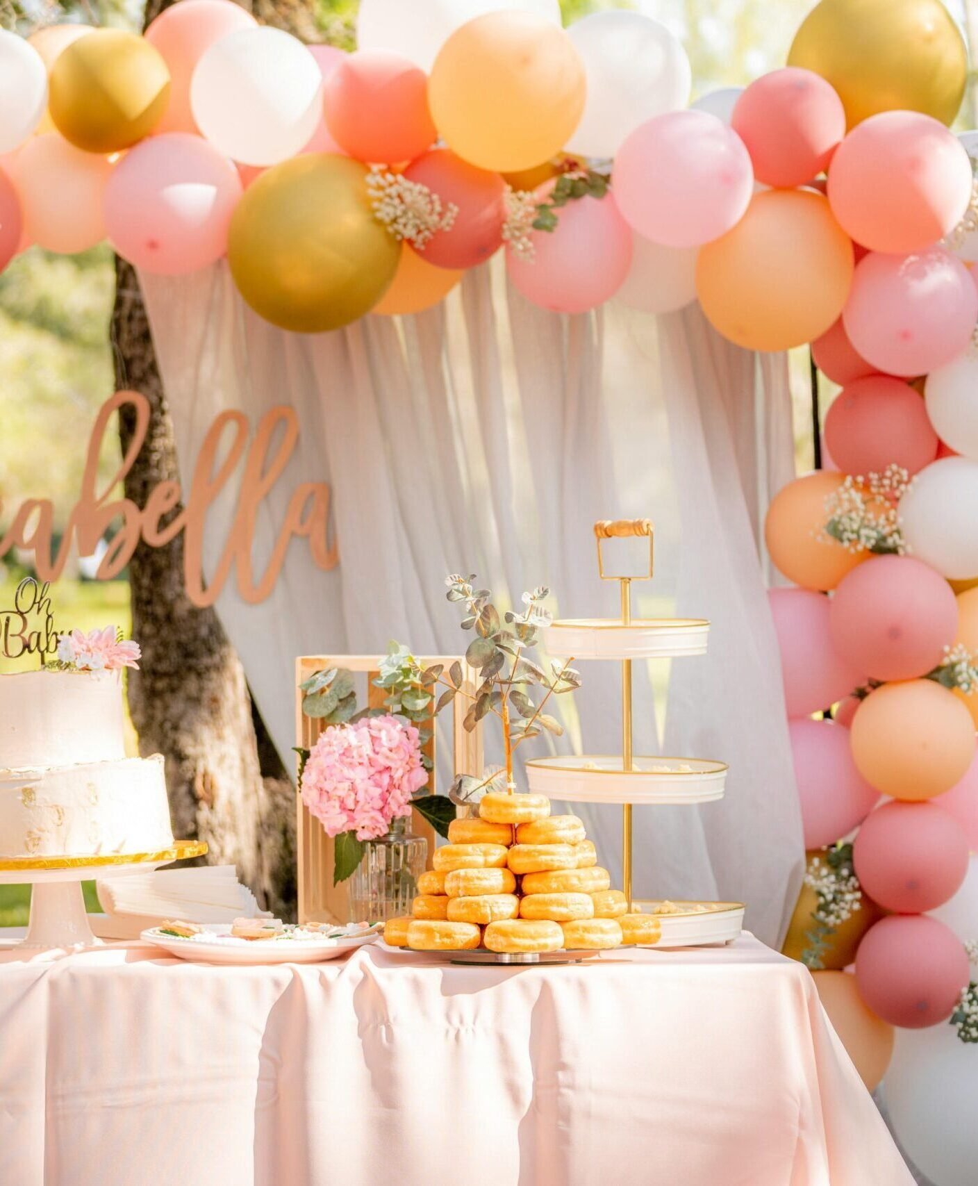 Delightful baby shower table with cake, balloons, and dessert display in an outdoor garden setting.